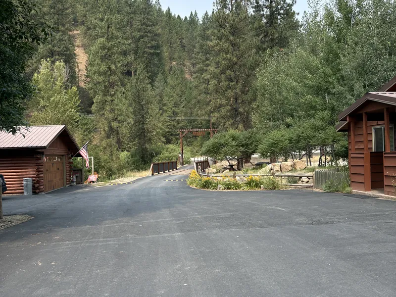 The paved entry drive passing between two log cabins on the way in from the gated bridge.